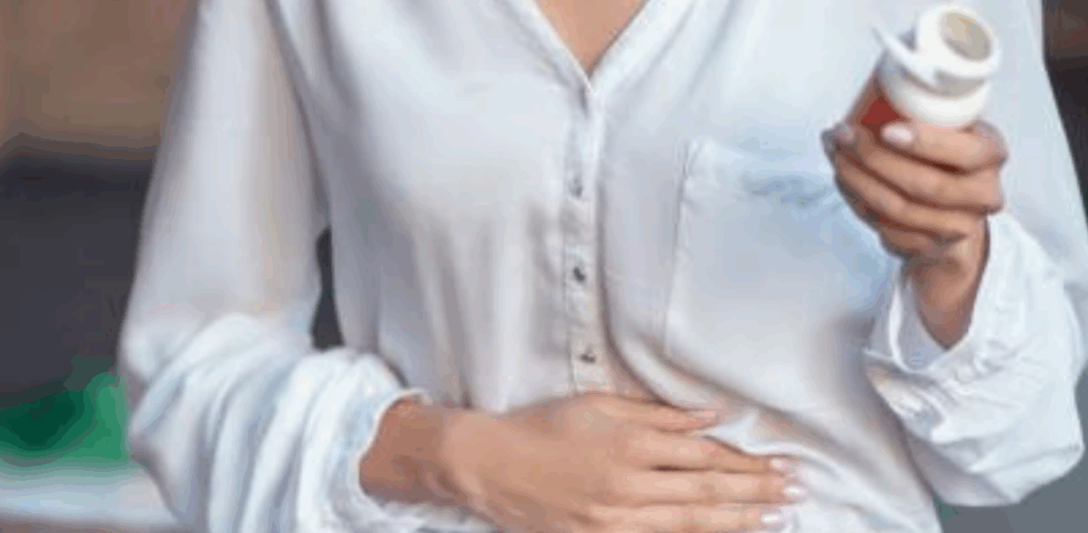 Woman holding stomach with one hand and a pill bottle in the other, suggesting digestive discomfort