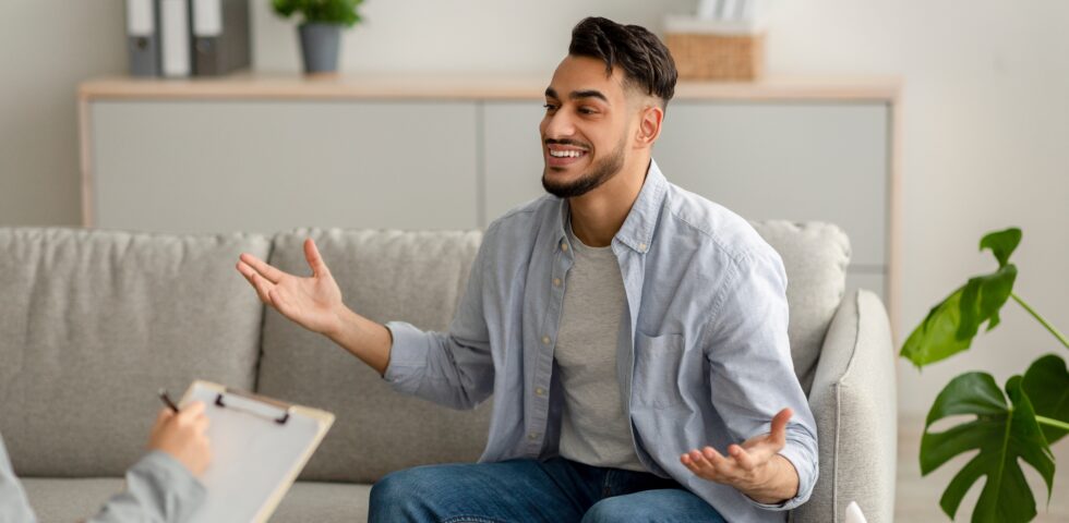 Man smiling and gesturing while talking to a therapist taking notes