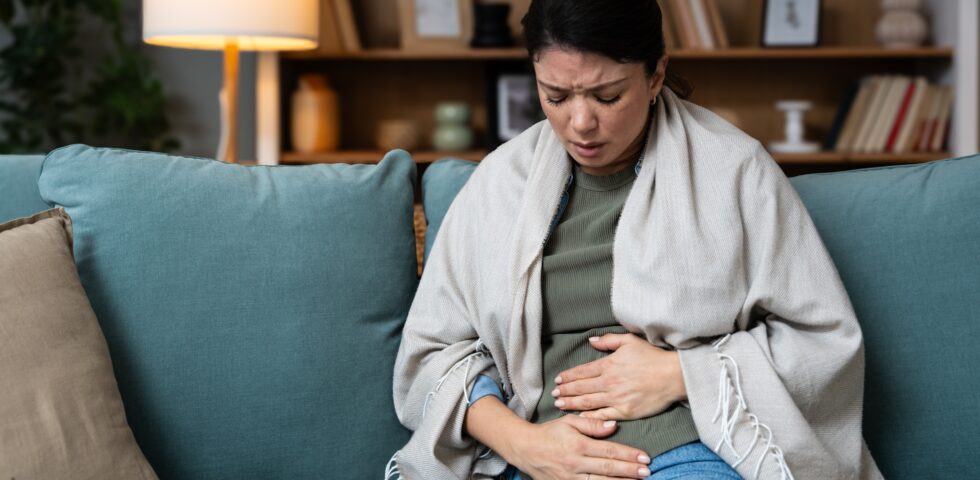 Woman sitting on a couch holding her stomach in pain